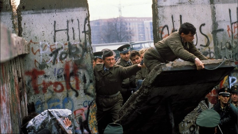 Люди разрушают Берлинскую стену в 1989 году, символ завершения холодной войны.